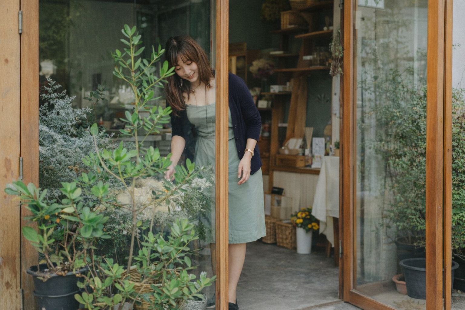 En kvindelig butiksejer passer planter ved indgangen til sin lille forretning.