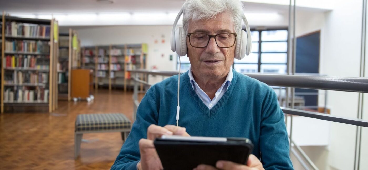 Ældre mand lytter med hovedtelefoner og bruger en tablet på biblioteket